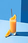 Squeezed orange juice garnished with orange slice on blue background