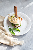 Hoher Winkel eines Tellers mit gesundem Toast mit Spiegelei-Pesto-Sauce und grünen Kräutern auf einem grauen Tisch beim Frühstück