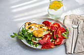 Teller mit leckerem, gesundem Mittagessen, bestehend aus Spiegeleiern mit Tomatenscheiben, Petersilie, Frühlingszwiebeln und Kapern, serviert mit einem Glas kaltem, reinem Wasser und Zitronenscheiben