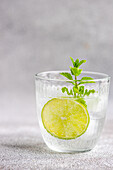 Glas Sommerlimonade mit Tonic und frischen Limetten- und Minzblättern auf grauer Oberfläche während der Sommersaison zu Hause