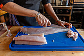 Hand of unrecognizable male chef wearing apron slicing raw fish fillet on chopping board during cooking delicious fish dish in restaurant at Zermatt Switzerland