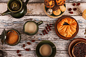 Top view of a wooden table set with cups of tea, a teapot, pie, and scattered dried leaves, evoking a cozy autumnal atmosphere.