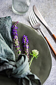 High angle of autumnal table setting with marbled plate, napkin, fork and knife and lavender flowers against gray surface
