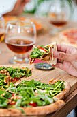 Selektiver Fokus der Ernte Person essen appetitlich Pizza mit Käse und Salat auf Holztisch mit Gläsern von Wein