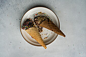 High angle waffle cones with coffee and chocolate ice cream with multicolored sugar and nuts on a ceramic plate