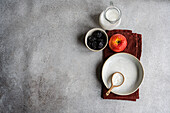 Draufsicht auf eine Schale mit Rosinen auf einem grauen Tisch neben einem leeren weißen Teller und einem Löffel, einem Apfel und einem Milchkännchen