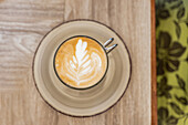 Top view closeup of hot coffee with creative latte art served in cup with saucer on wooden table at cafe