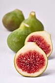 Vibrant fresh figs with one sliced in half, showcasing the red interior against a clean, white backdrop.
