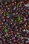 Top view of metal baking pan with fresh ripe black grapes placed on parchment paper in kitchen