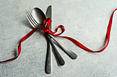 Hoher Winkel von Vintage-Besteck auf grauer Oberfläche mit roter Schleife in heller Küche
