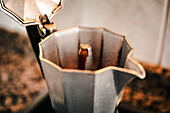 Nahaufnahme einer Espressomaschine aus Edelstahl auf einem glatten Kochfeld mit einer kunstvoll gefliesten Aufkantung, die einen kontrastreichen Hintergrund bildet und die Verlockung von selbst gebrühtem italienischen Kaffee unterstreicht