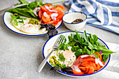 A nutritious keto meal consisting of leafy greens, avocado, eggs, and tomatoes, served on a white plate with a blue rim.