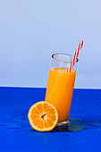 Close up shot of glass of orange juice cocktail and fresh slice of orange on blue background