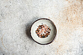 Schüssel mit Salatgewürzmischung bestehend aus rosa Himalaya-Salz, Leinsamen, Sesam und schwarzem Pfeffer vor einem Betonhintergrund