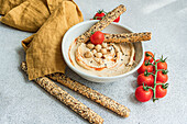 High angle of healthy plant-based plate with hummus and tomatoes served with bread sticks in bowl near napkin against blurred background