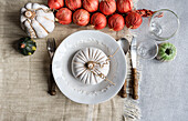 Draufsicht auf einen herbstlich gedeckten Tisch mit weißem Kürbis auf einem Teller, der neben Besteck, Gläsern und roten Zwiebeln auf dem Tisch steht