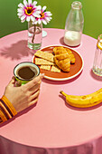 Unrecognizable person drinking hot aromatic coffee in cup placed on table with delicious croissants and banana decorated by flowers in vase