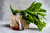 Lebendiger Blattspinat in einer rustikalen Holzkiste, gepaart mit einer eleganten Glaskaraffe mit Olivenöl als Symbol für frische Salatzutaten und deren Zubereitung