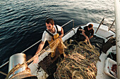 Von oben fokussierter bärtiger männlicher Fischer in Uniform, der mit einem Netz auf Fischfang geht, während er auf einem Schoner in Soller nahe der Baleareninsel Mallorca arbeitet