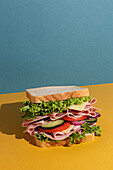 Delicious sandwich with ham, tomatoes, cucumber and cheese slices and fresh lettuce on blue and yellow background