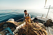 From above focused bearded male fisher in uniform seiner hunting fish with net while working on schooner in Soller near Balearic Island of Mallorca