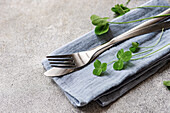 Close up of table setting with leaves of shamrock plant on napkin with fork and knife against concrete background