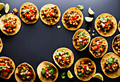 Top view of many tacos filled with chopped tomatoes over meat with chickpeas and cilantro on top served on black background. Generative AI