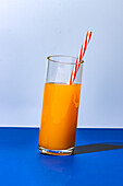 Close up shot of glass of fresh orange juice cocktail on blue background