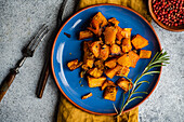 Baked spicy pumpkin cubes served on blue ceramic plate on the table