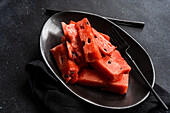 Top view of pieces watermelon on a black plate placed on a dark concrete background