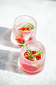 Blick von oben auf sonnenbeschienene Gin-Tonic-Cocktails mit Granatapfel und Rosmarin in strukturierten Gläsern auf einer hellen Fläche