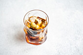 High angle of transparent glass cup with whiskey alcoholic drink and stick of olives cocktail with ice cubes on grey background in studio