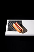 High angle of appetizing bun with sausage and ketchup served table mat over white wooden board against black background in studio