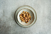 A ceramic bowl filled with mixed nuts is centered on a textured grey surface, offering a minimalist and organic aesthetic