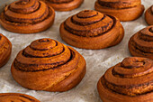 Nahaufnahme einer Sammlung frisch gebackener, knuspriger Zimtrollen auf einem hellen Marmortisch in einer Bäckerei