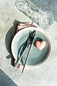 Top view of ceramic plate with cutlery and napkin with heart shaped decor crystal placed on concrete surface at kitchen table for meal during Valentine's day celebration