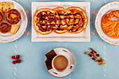 A top-view of a continental breakfast setup featuring pastries, cereal, fresh fruit, and beverages, laid out on a blue surface.