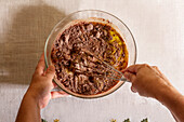 Top view of Hands of anonymous person using a whisk to mix chocolate batter in a clear glass bowl on a kitchen table