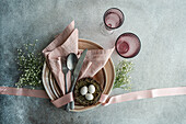 Top view of an Easter table setting featuring a nest with eggs, surrounded by ceramic dishes, cutlery, and pastel linens.