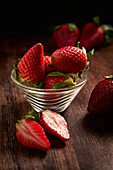 Köstliche frische Erdbeeren mit grünen Blättern in einer transparenten Schale auf einem Holztisch
