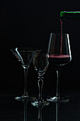 Elegant red wine pouring into a glass amidst empty stemware against a dark backdrop