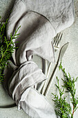 Top view of Christmas composition of fork and knife together in handkerchief near green fir sprigs placed on gray background