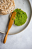Top view of rice bread on a plate with spread vibrant green spinach pesto pasta-sauce, set against gray backdrop