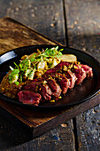 High angle of appetizing traditional Ecuadorian dish made of roasted meat with sauce herbs and vegetables served on black plate on cutting board