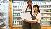 Cheerful multiethnic colleagues in aprons surfing on laptop together while working in contemporary store and checking information during work process