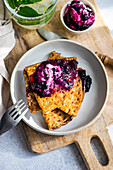 Golden crepes topped with blueberry jam and a dollop of sour cream, served on a rustic wooden board.