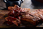 High angle of appetizing grilled pork ribs with sauce served on wooden board in kitchen against blurred background