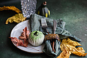 Hohe Winkel der herbstlichen Tisch mit Serviette, Messer und Gabel Platz auf dem Teller in der Nähe von bunten Blättern, kleine Kürbisse und leere Glas gegen dunkle Oberfläche