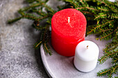 From above of candles placed on gray ceramic surface near green twigs of fir as symbol of Christmas