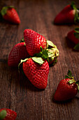 Composition of fresh appetizing strawberries with green leaves arranged in heap on wooden surface